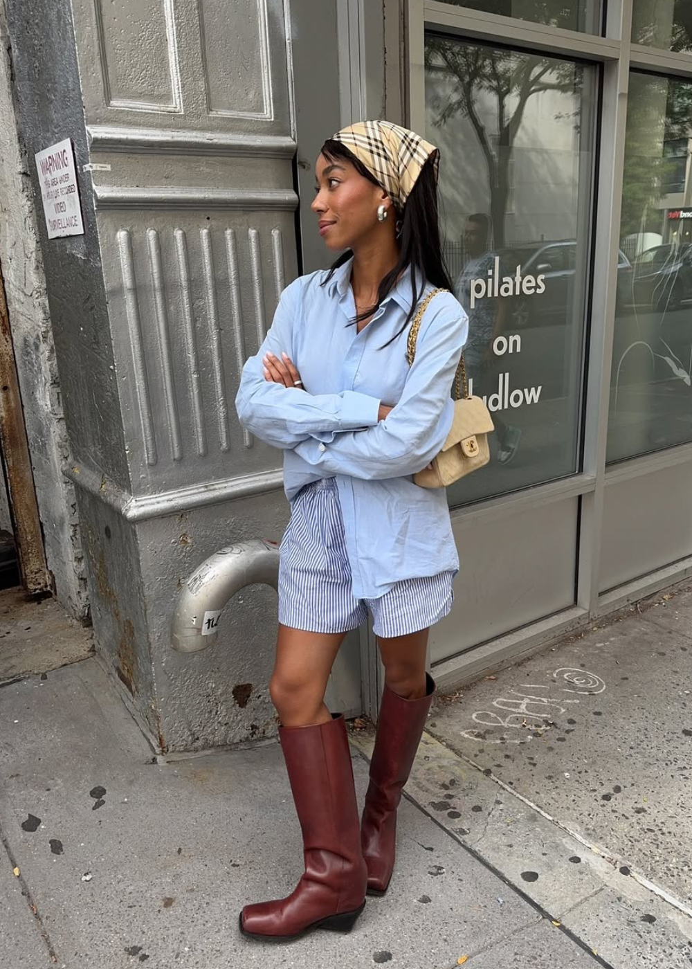 Looks com camisa azul feminina: modelo posa com short listrado, botas vinho e lenço xadrez.