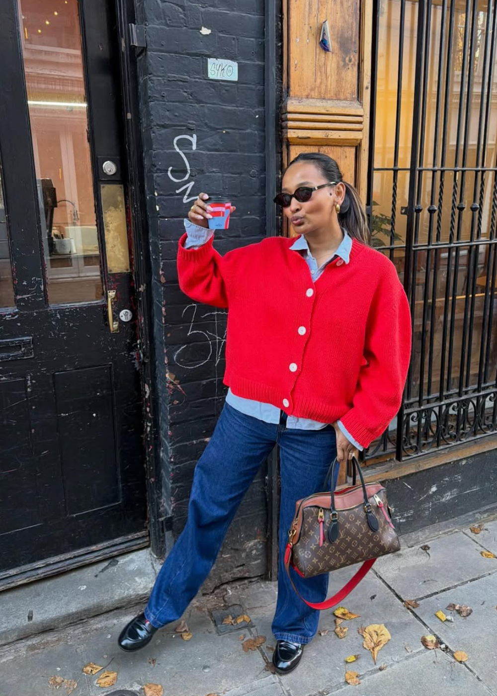 Looks com camisa azul feminina: modelo posa com cardigan vermelho, jeans reto e mocassim preto em clima urbano descontraído.
