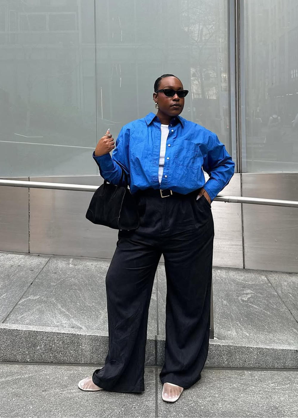 Looks com camisa azul feminina: modelo posa com alfaiataria preta ampla, regata branca e bolsa preta em clima urbano