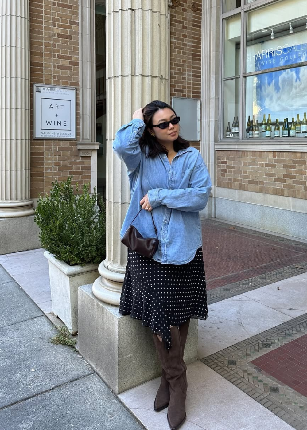 Looks com camisa azul feminina: modelo posa com denim amplo, saia poá e bota marrom.