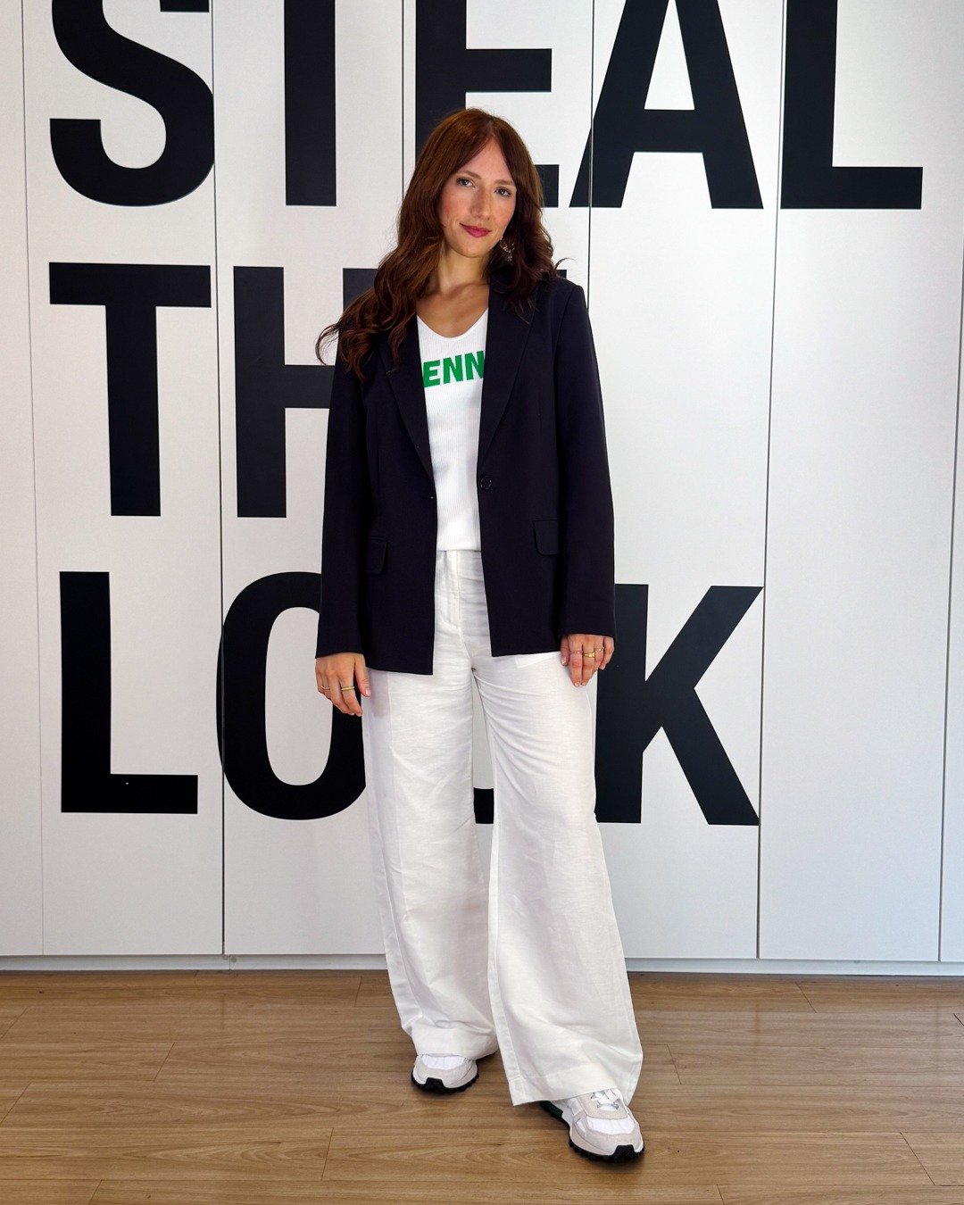 Modelo posa com tênis versátil e estiloso, blazer preto e calça branca ampla em cenário gráfico. Texto: STEAL THE LOOK