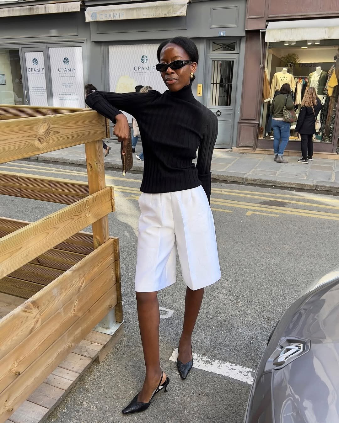 Modelo posa com tricô canelado preto e bermuda branca de alfaiataria - melhores perfumes femininos de outono