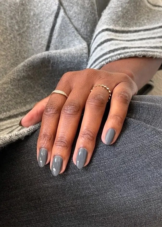 Unhas mais populares em cinza brilhante oval, mão posa com anéis delicados sobre look de tricô e jeans em clima elegante.