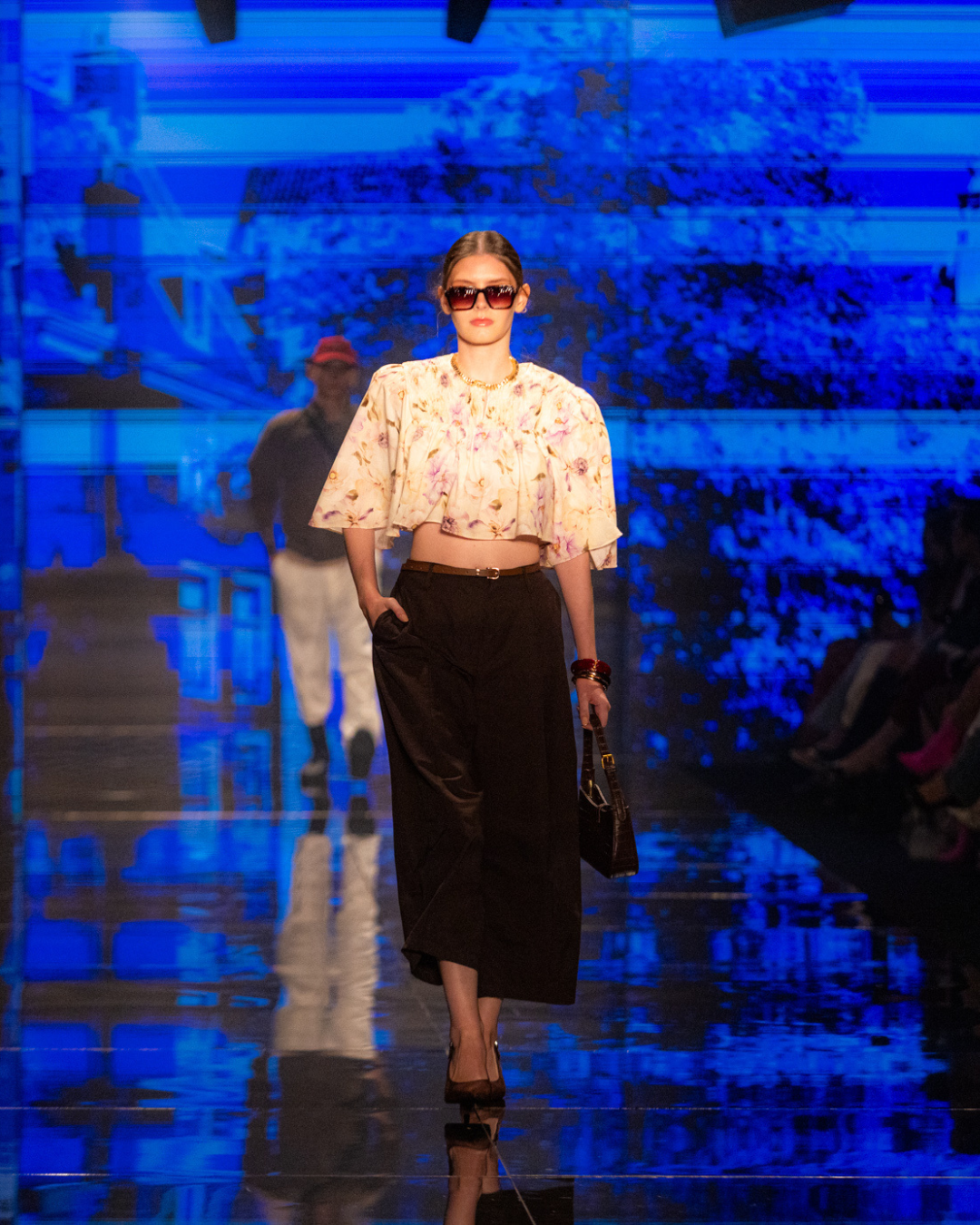 Modelo posa na passarela com blusa floral ampla, calça preta fluida e azul,cores e estampas tendência do outono inverno 2026