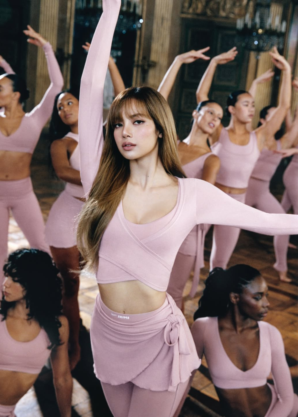 Rosa pastel em looks de dança ajustados; modelo posa com braço erguido em salão clássico elegante.