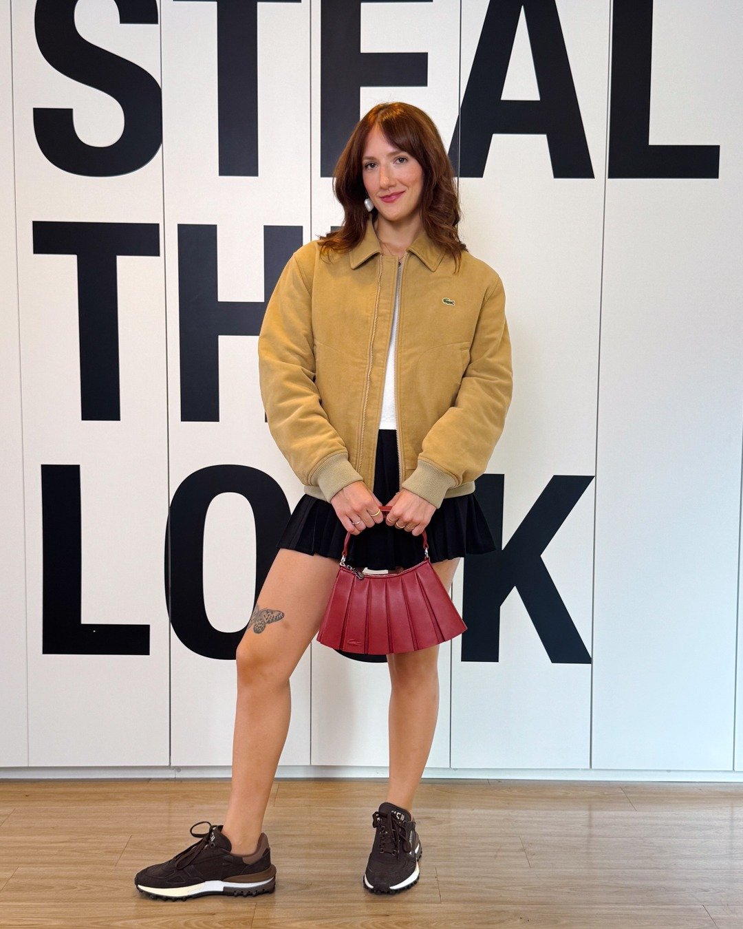 Modelo posa com tênis versátil e estiloso, jaqueta bege, saia preta plissada e bolsa vinho; Texto: STEAL THE LOOK
