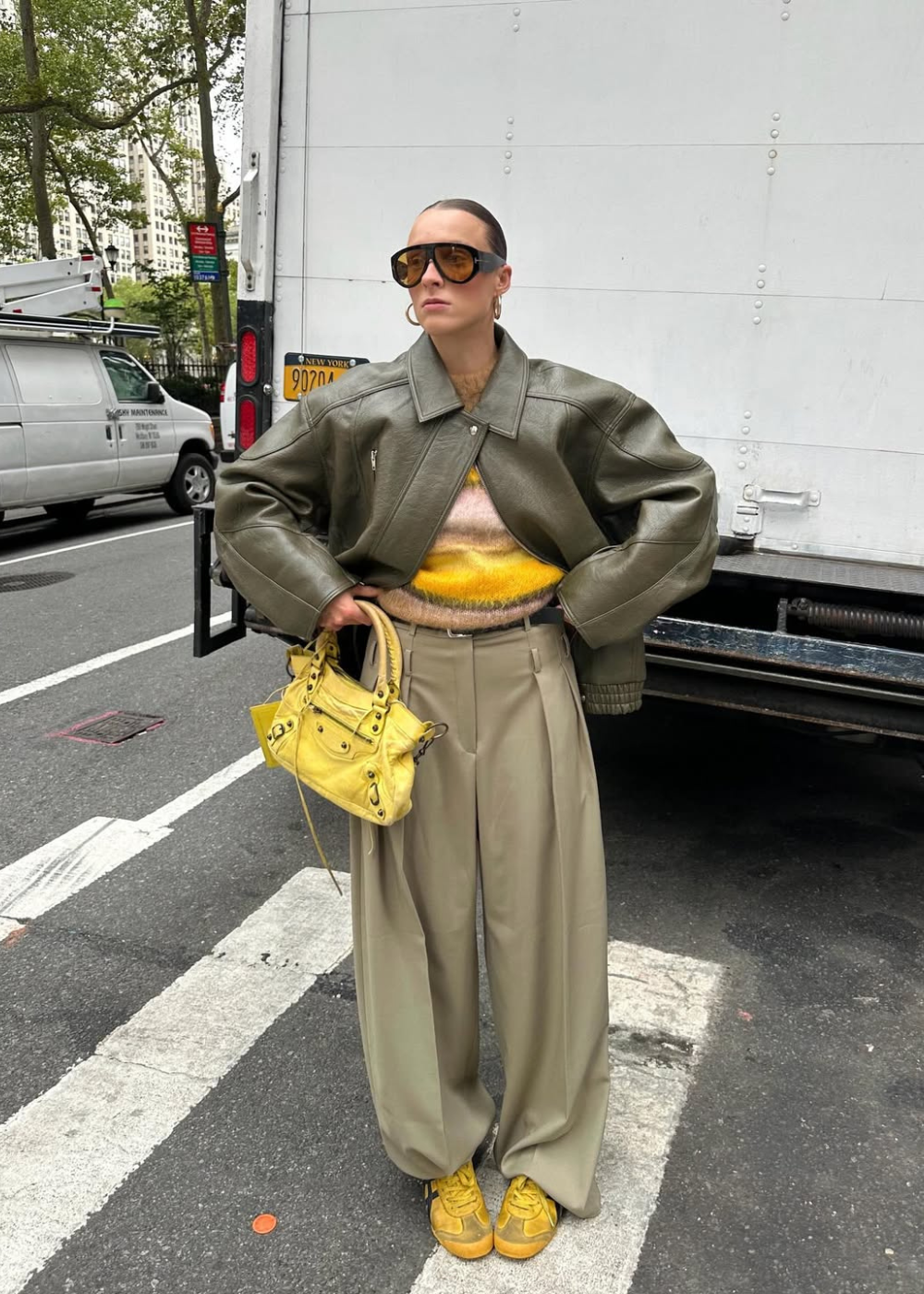 Sapatos do inverno 2026: modelo posa com tênis amarelos, jaqueta de couro oversized e alfaiataria bege em clima urbano