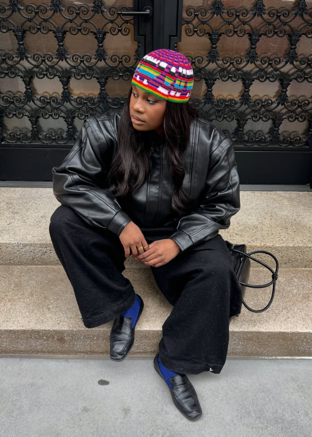 Sapatos do inverno 2026 com mocassim preto e meia azul; modelo posa sentada com jaqueta de couro e gorro colorido.