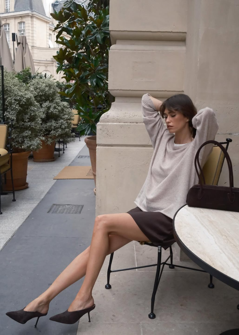 Sapatos do inverno 2026 com mule de salto fino marrom, tricô bege e saia reta em café, modelo posa com elegância serena.