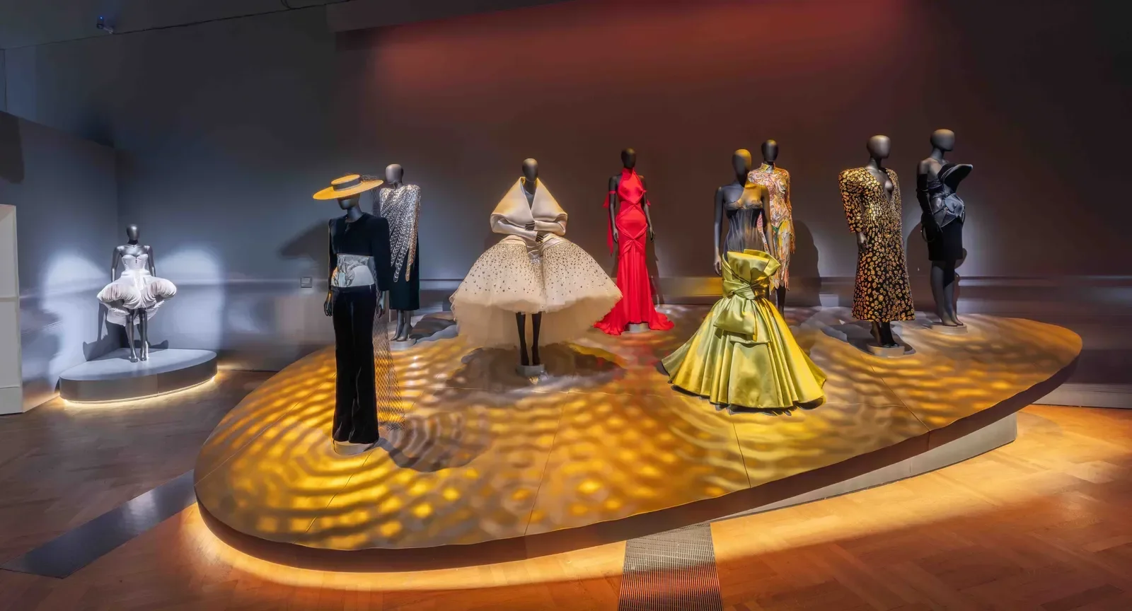 Exposição da Schiaparelli reúne vestidos escultóricos em branco, vermelho, dourado e preto sob luz dramática e aura surreal.