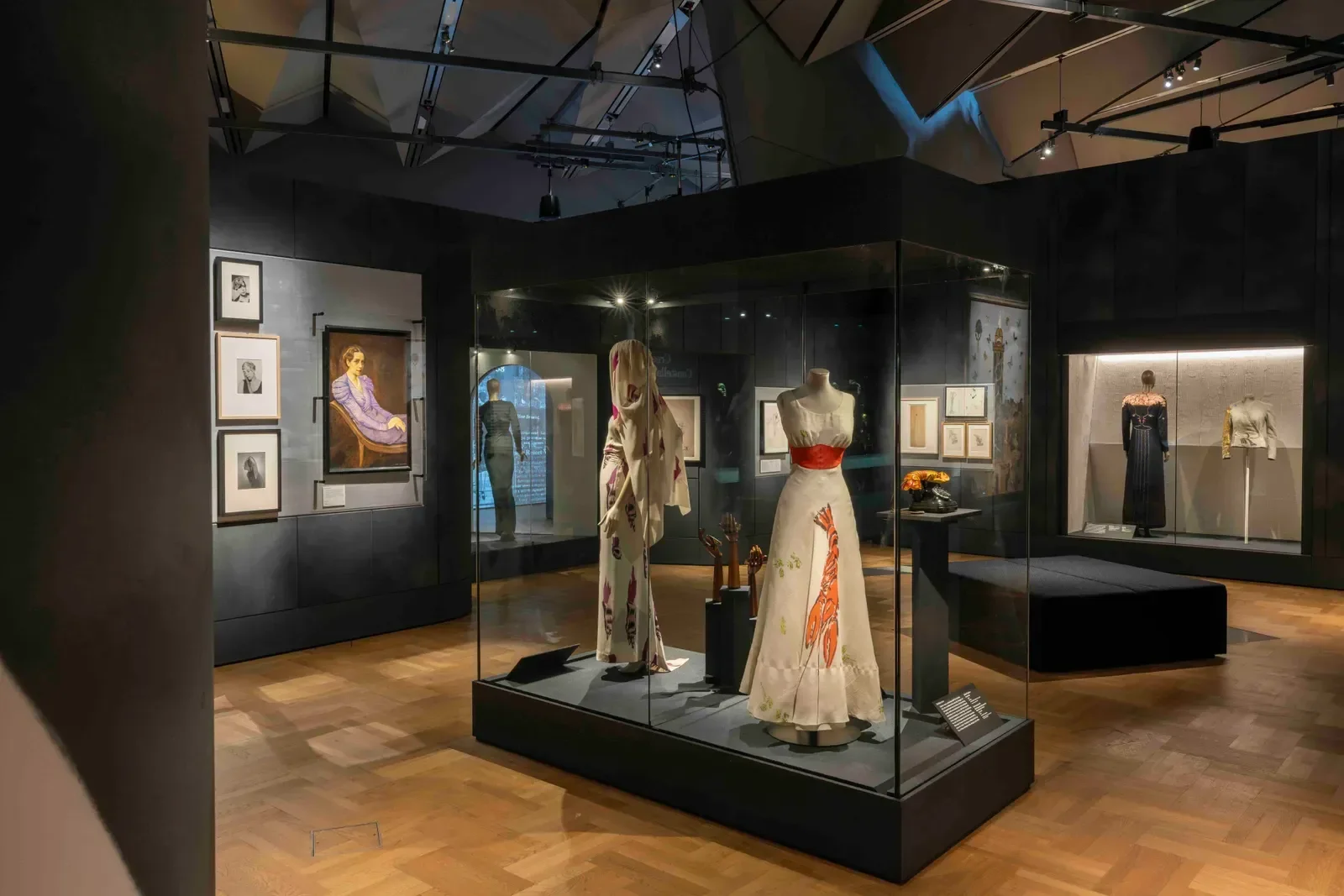 Exposição da Schiaparelli com vestidos bordados em branco, preto e vermelho em vitrines, clima elegante e contemplativo