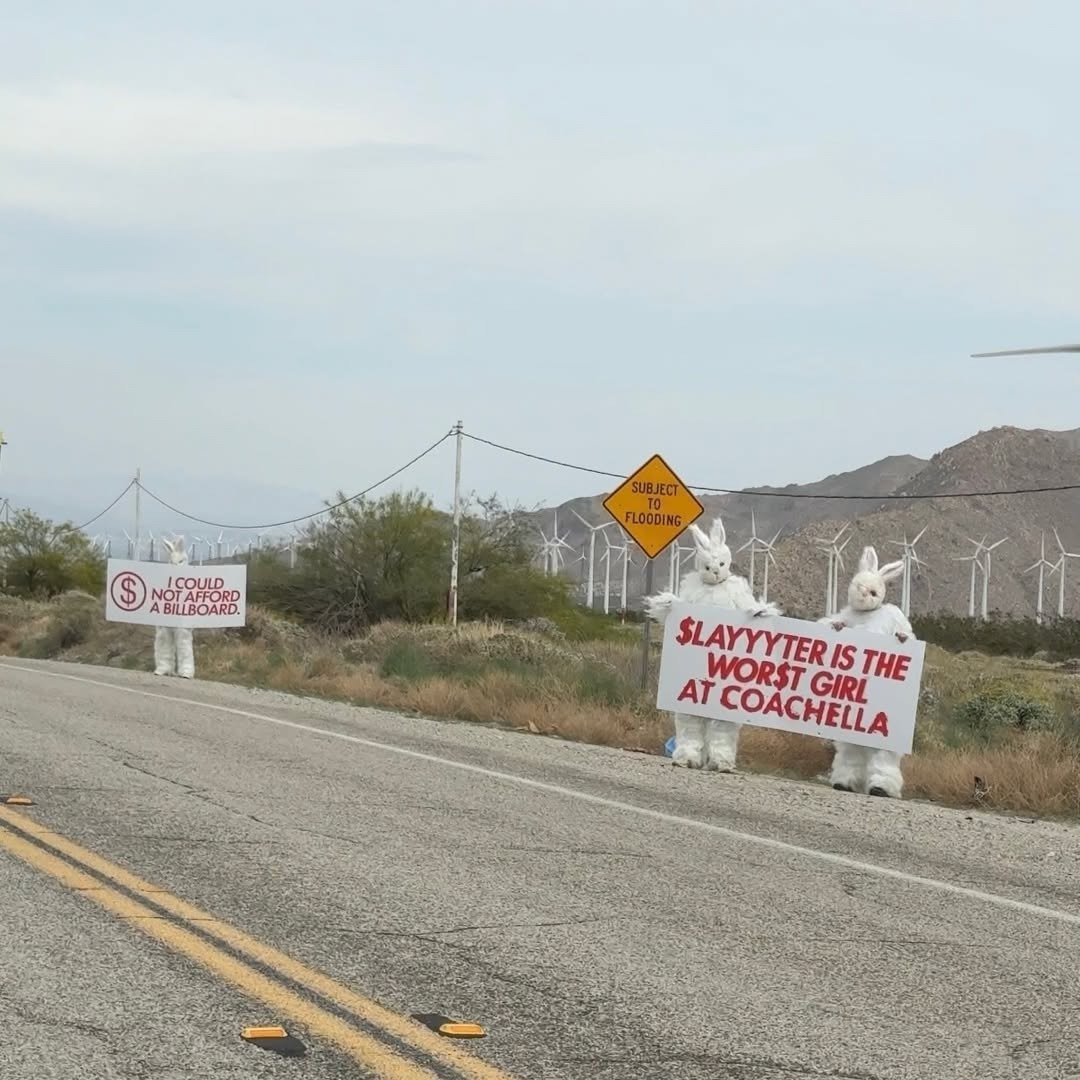 Slayyyter surge com coelhos brancos à beira da estrada desértica, em clima provocador.