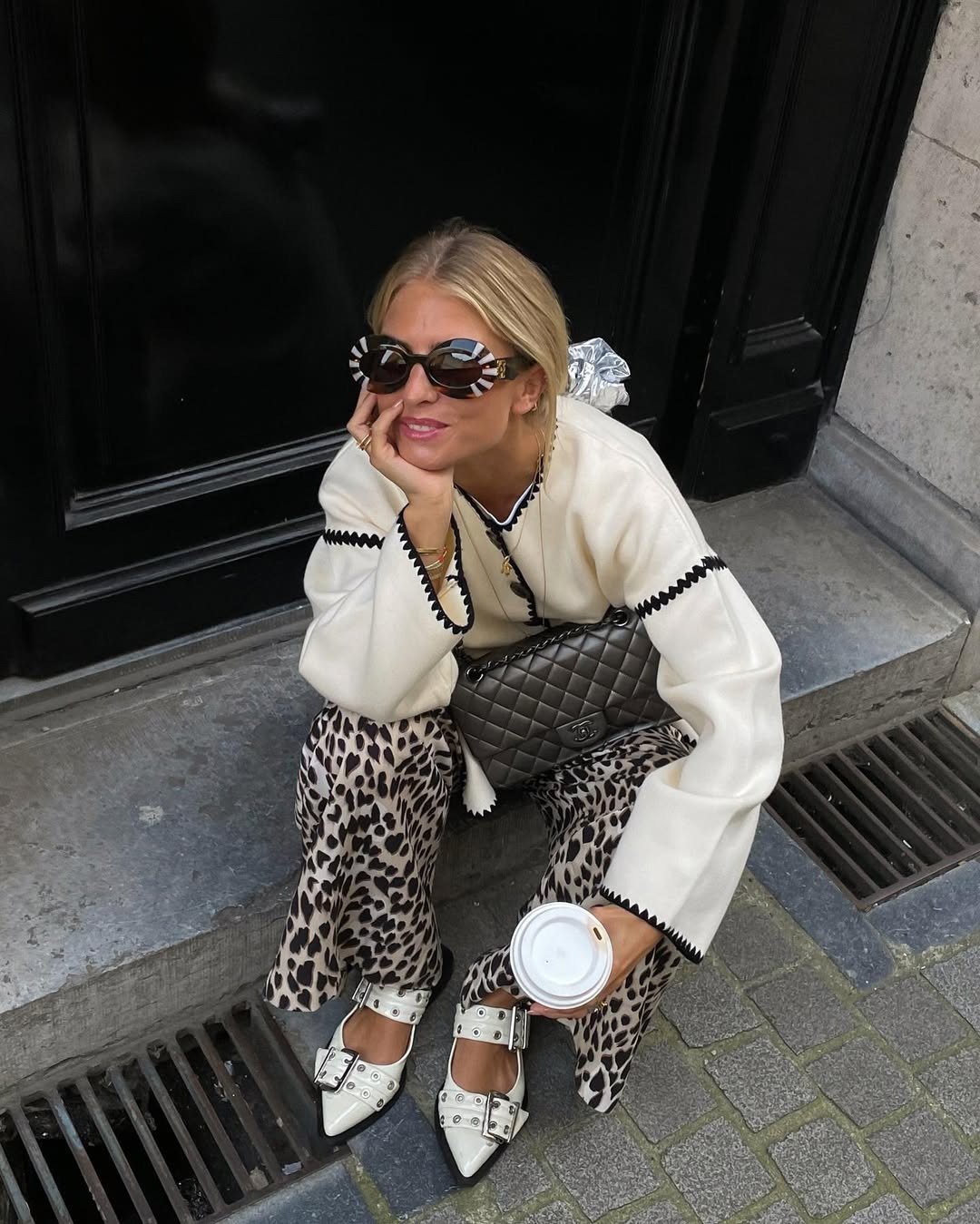 Melhores sapatos para o outono: modelo posa agachada com sapatilhas brancas de fivelas, tricô creme e calça animal print.