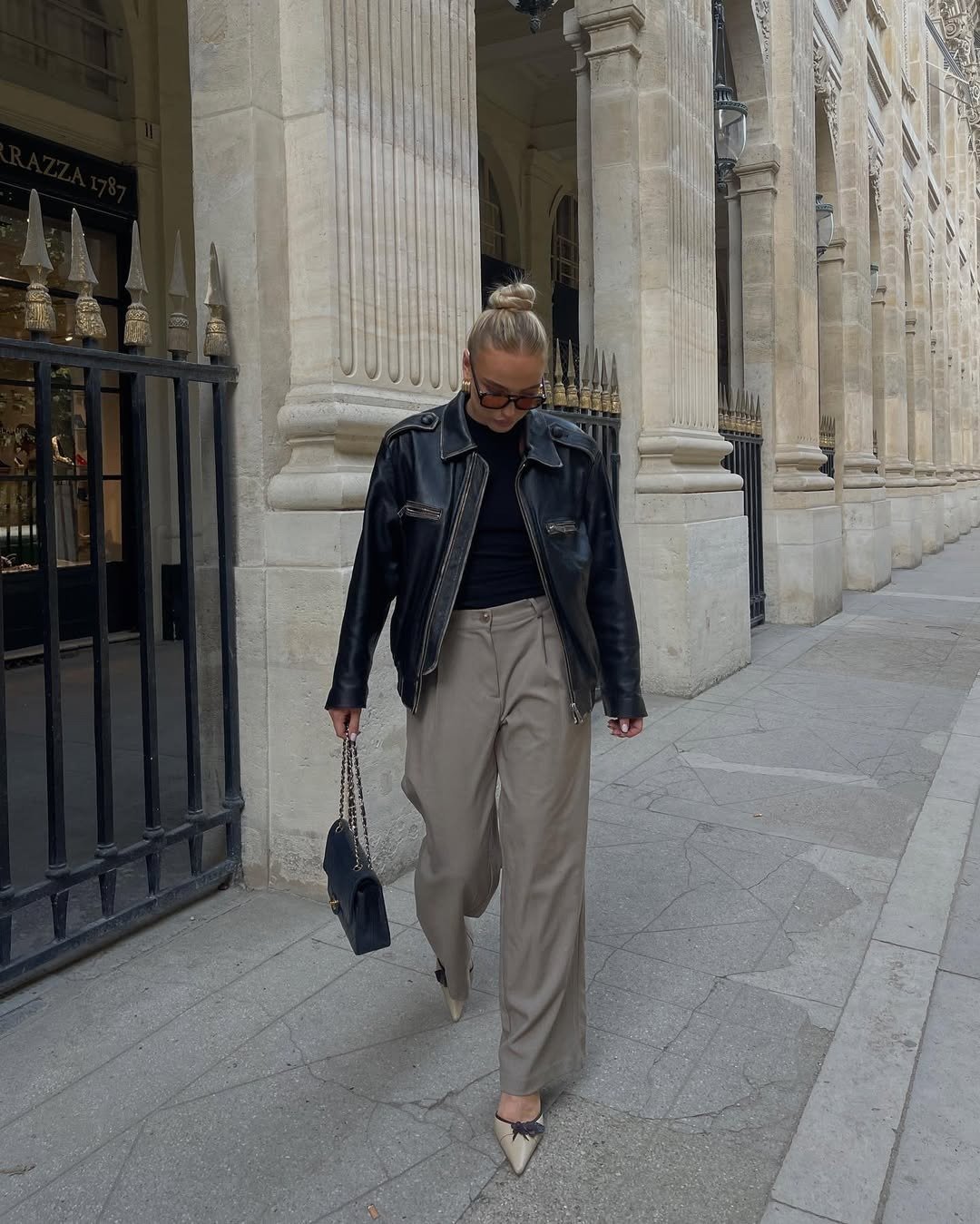 Modelos de calças de alfaiataria bege reta ganham destaque; modelo caminha com jaqueta preta em rua elegante e sóbria.