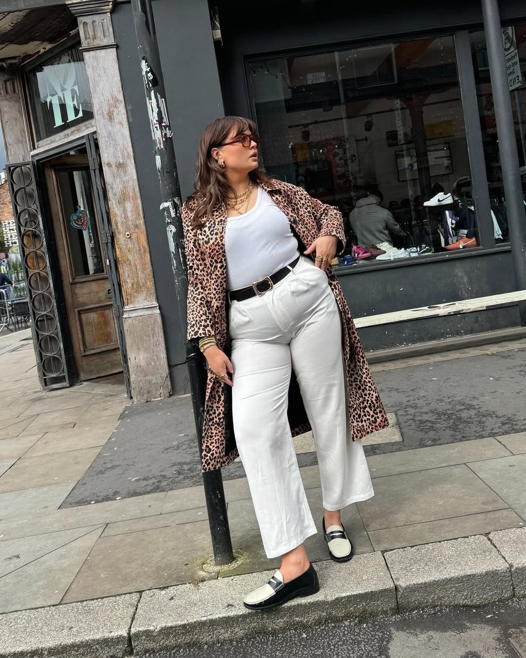 Modelo posa com calça branca ampla, regata canelada e casaco animal print na calçada, em estilo urbano marcante.