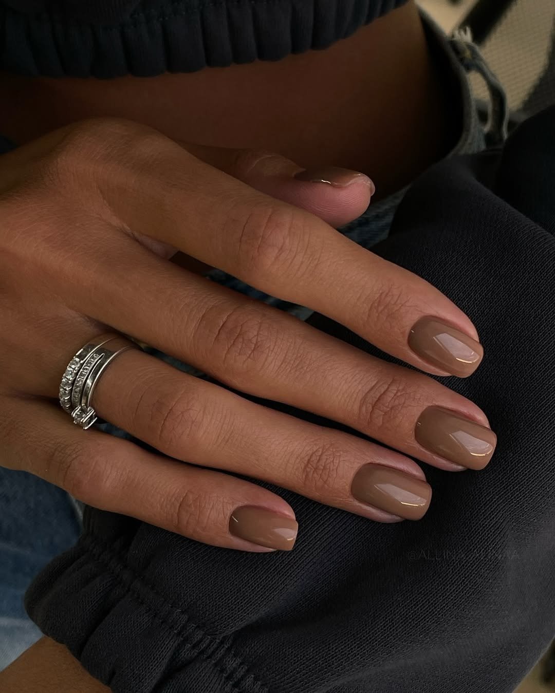 Unhas para madrinha de casamento em marrom taupe brilhante, curtas e ovais, com anel prateado e clima elegante.