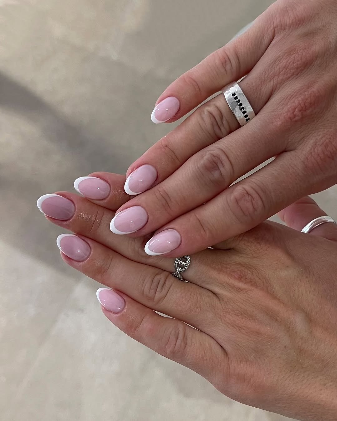 Unhas para madrinha de casamento com francesinha branca e base rosa-claro, formato amendoado e anéis prateados elegantes.