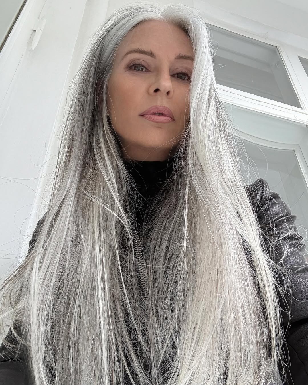 Melhor shampoo para cabelos grisalhos em destaque com modelo posa de casaco preto e fios longos prateados em luz suave.