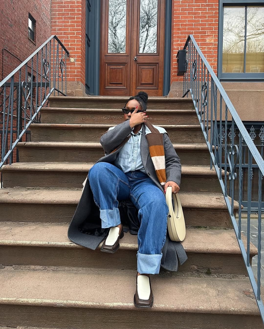 Melhores sapatos para o outono: modelo posa de jeans, casaco cinza e mules bicolor em escada urbana elegante.