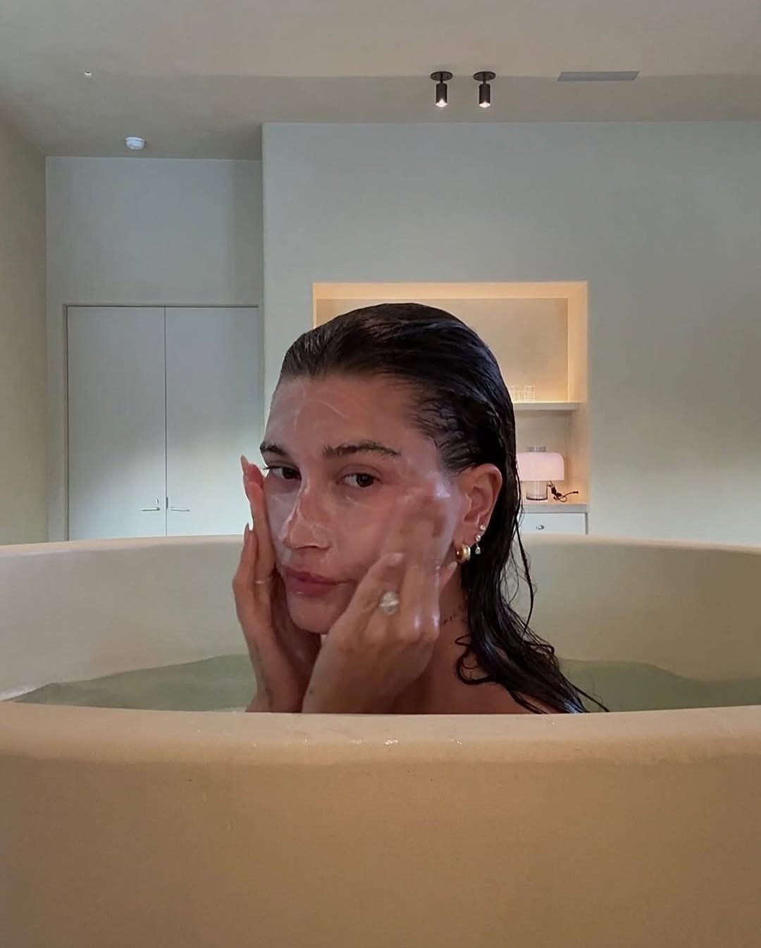Ácido mandélico para que serve: modelo relaxa na banheira bege, aplica máscara facial e cria clima de autocuidado sereno