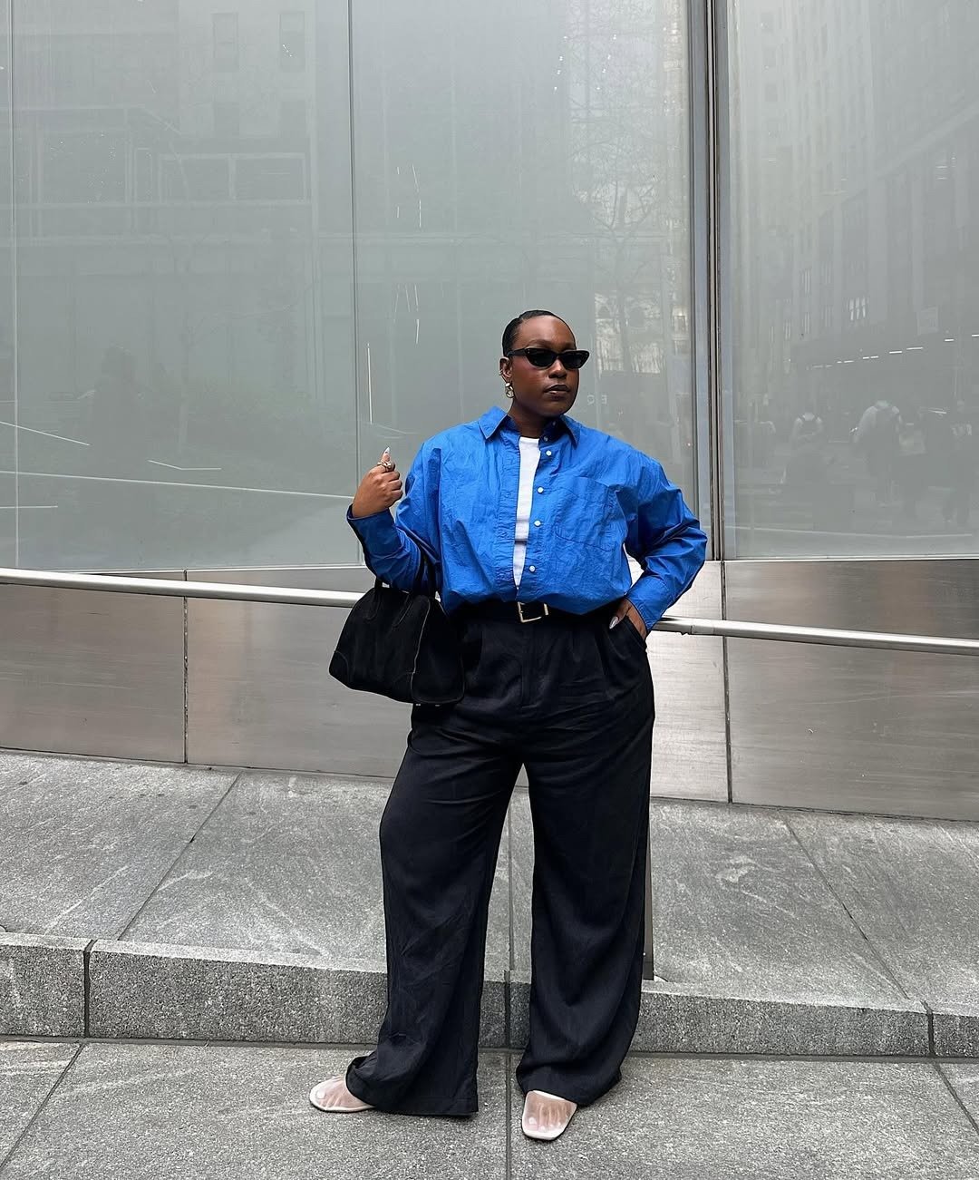 Modelos de calças de alfaiataria: modelo posa com camisa azul ampla, calça preta reta e elegância urbana sóbria.