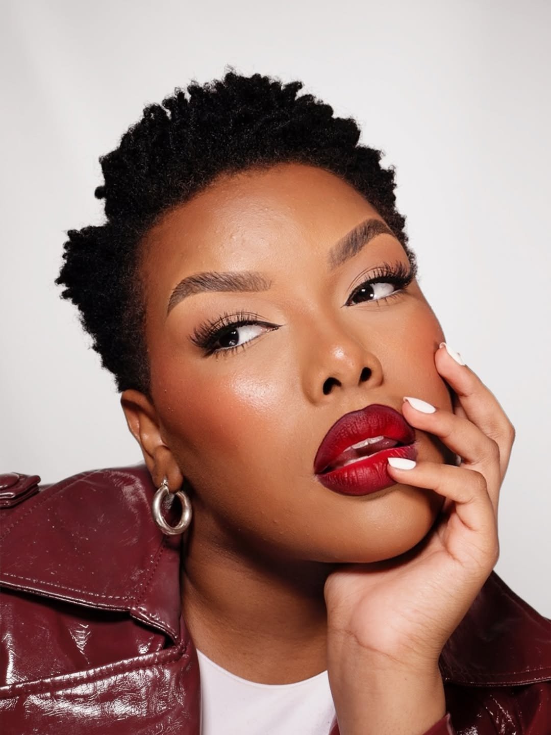 Modelo posa com jaqueta vinil vinho e argola prata; cores de batom vermelho intenso destacam beleza sofisticada.