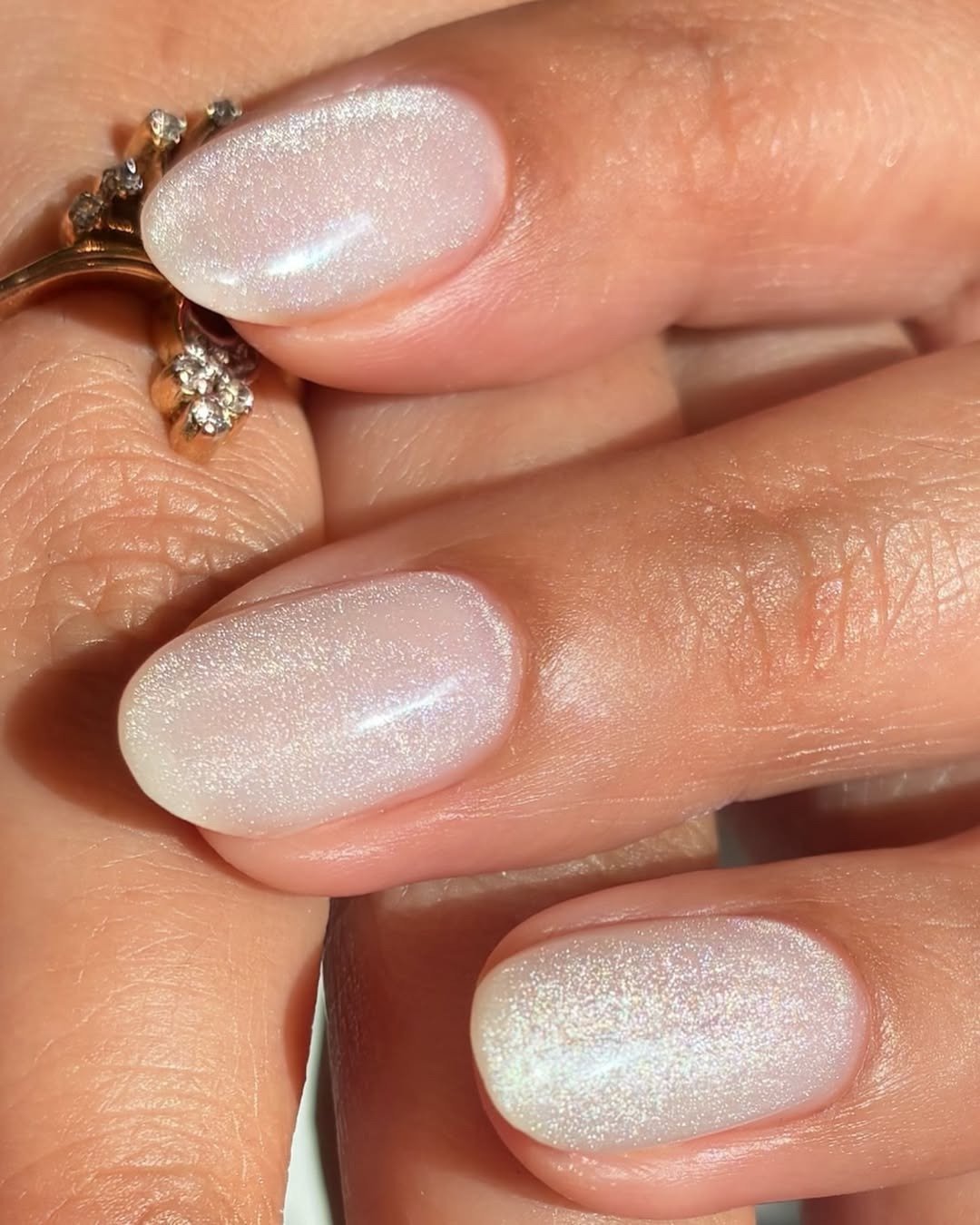 Unhas para madrinha de casamento com esmalte perolado branco leitoso, formato oval curto e brilho delicado ao lado de anel