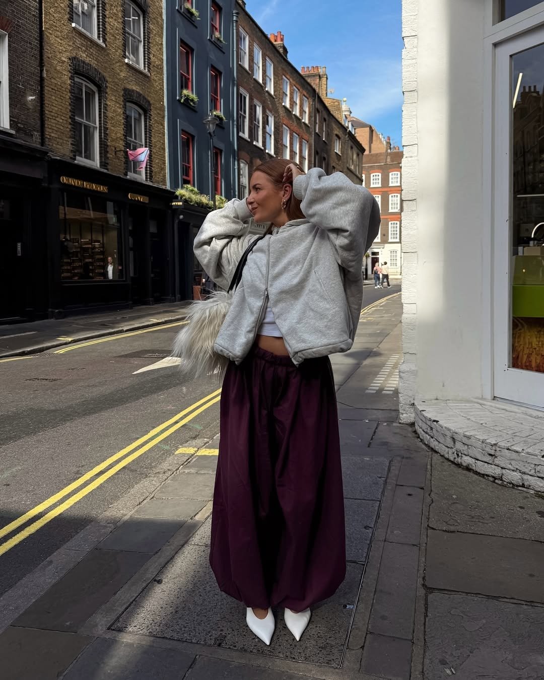 Looks estilosos para a variação de temperatura no outono: modelo posa com moletom cinza, calça vinho ampla e bolsa felpuda.