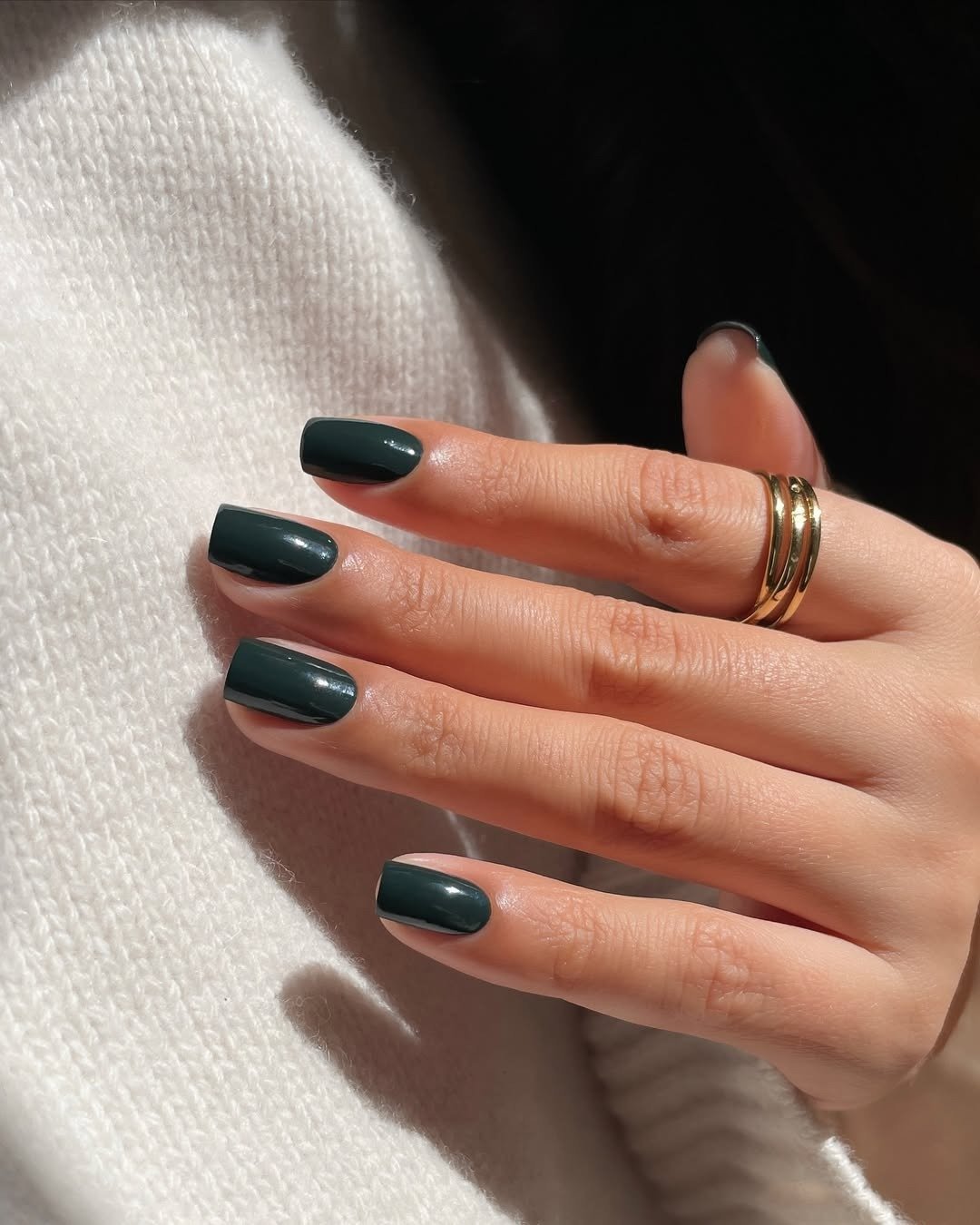 Unhas para madrinha de casamento em verde escuro brilhante com corte reto, anel dourado e tricô off-white elegante.