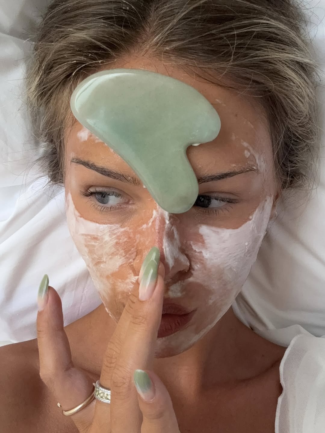 Ácido mandélico para que serve: modelo aplica skincare com máscara branca e pedra verde, clima de autocuidado sereno