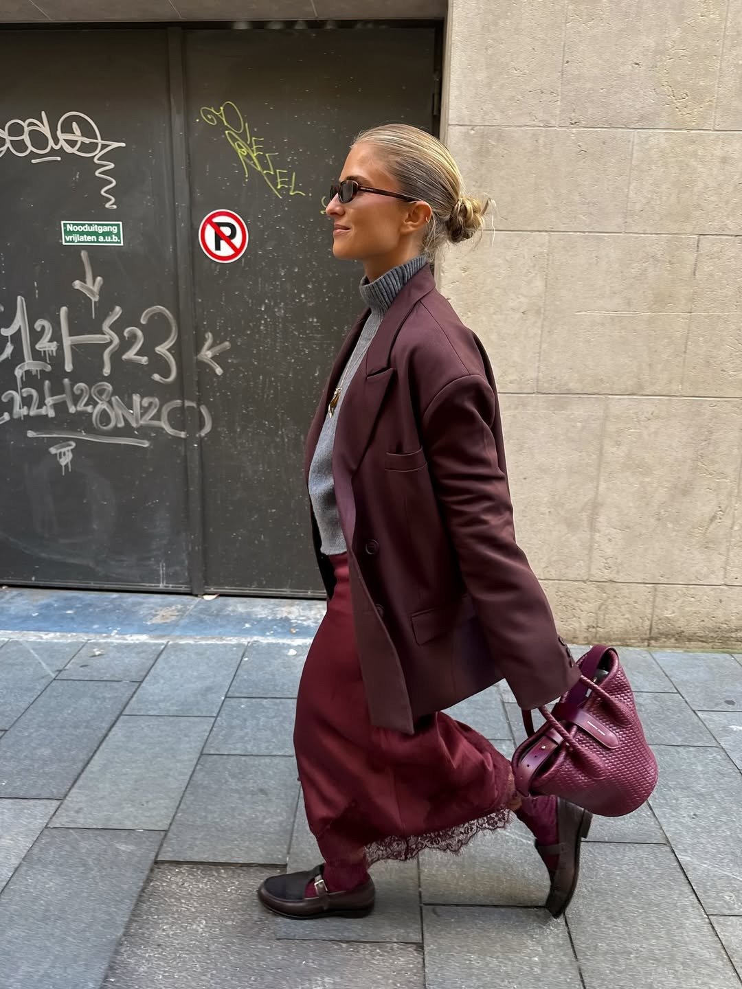 Looks estilosos para a variação de temperatura no outono: modelo caminha com blazer vinho, tricô cinza e saia rendada.