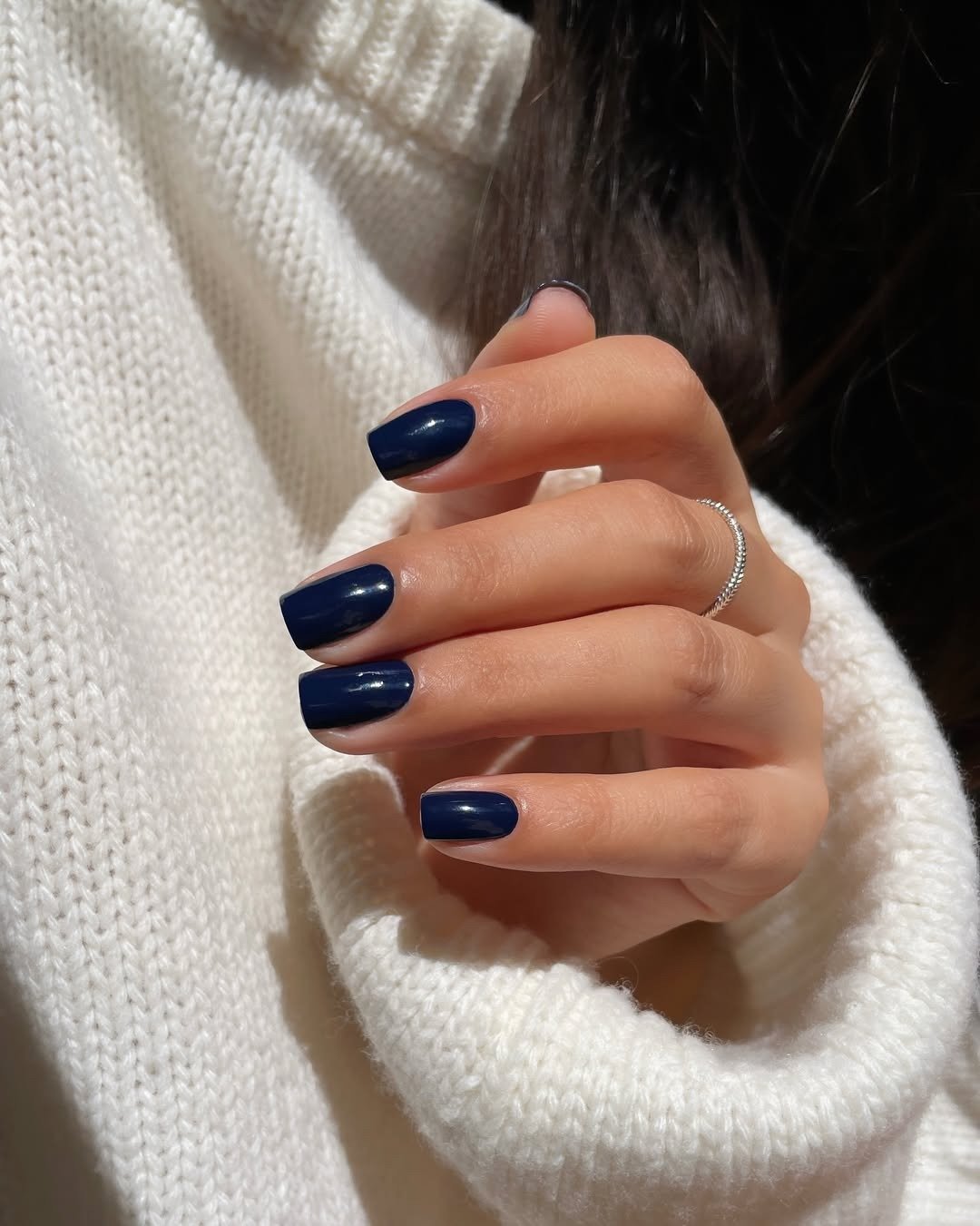 Unhas para madrinha de casamento em azul-marinho brilhante com suéter tricô branco e anel fino, em clima elegante.