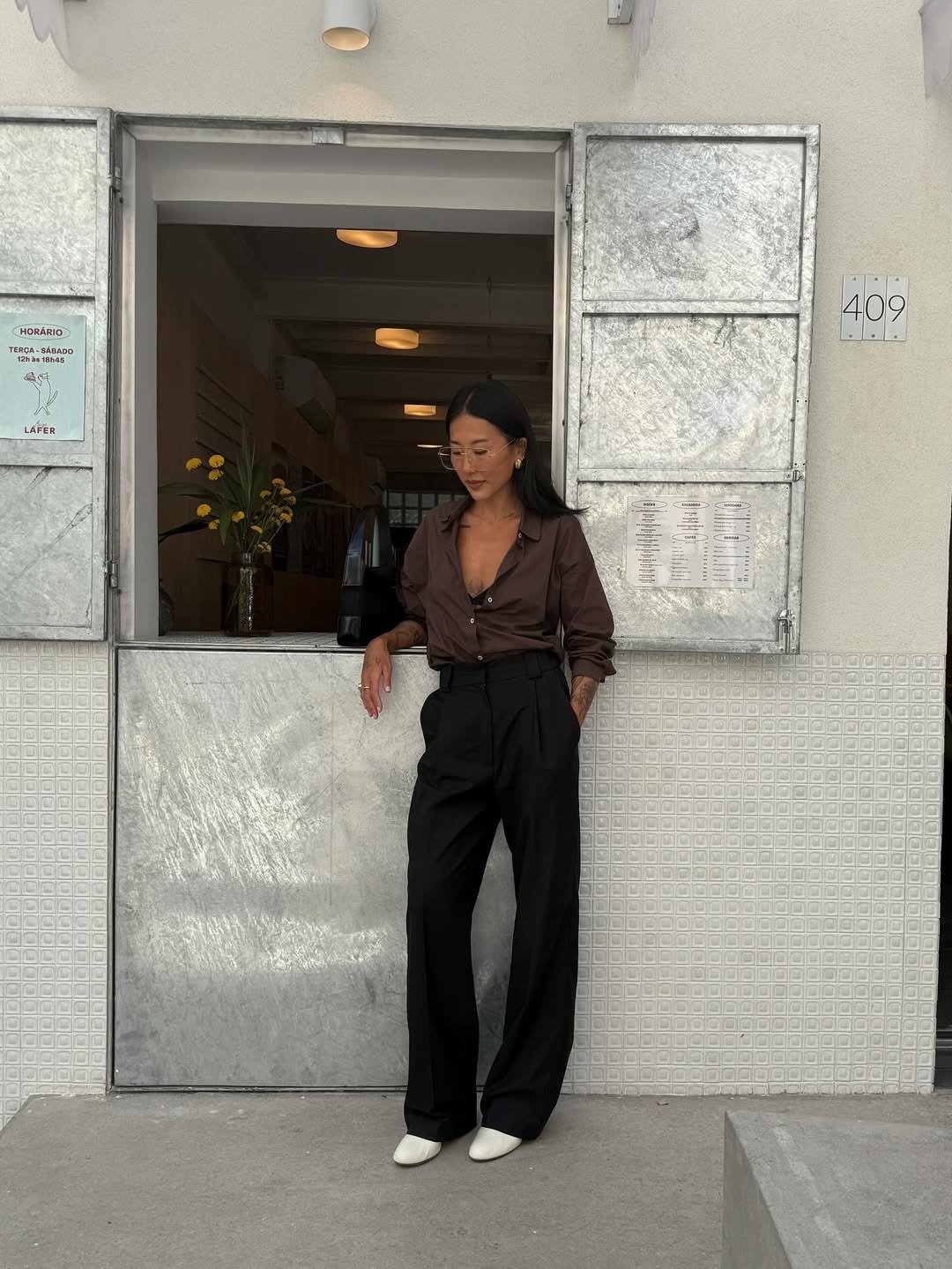 Modelos de calças de alfaiataria: modelo posa com cintura alta e pernas amplas, camisa marrom e elegância urbana.