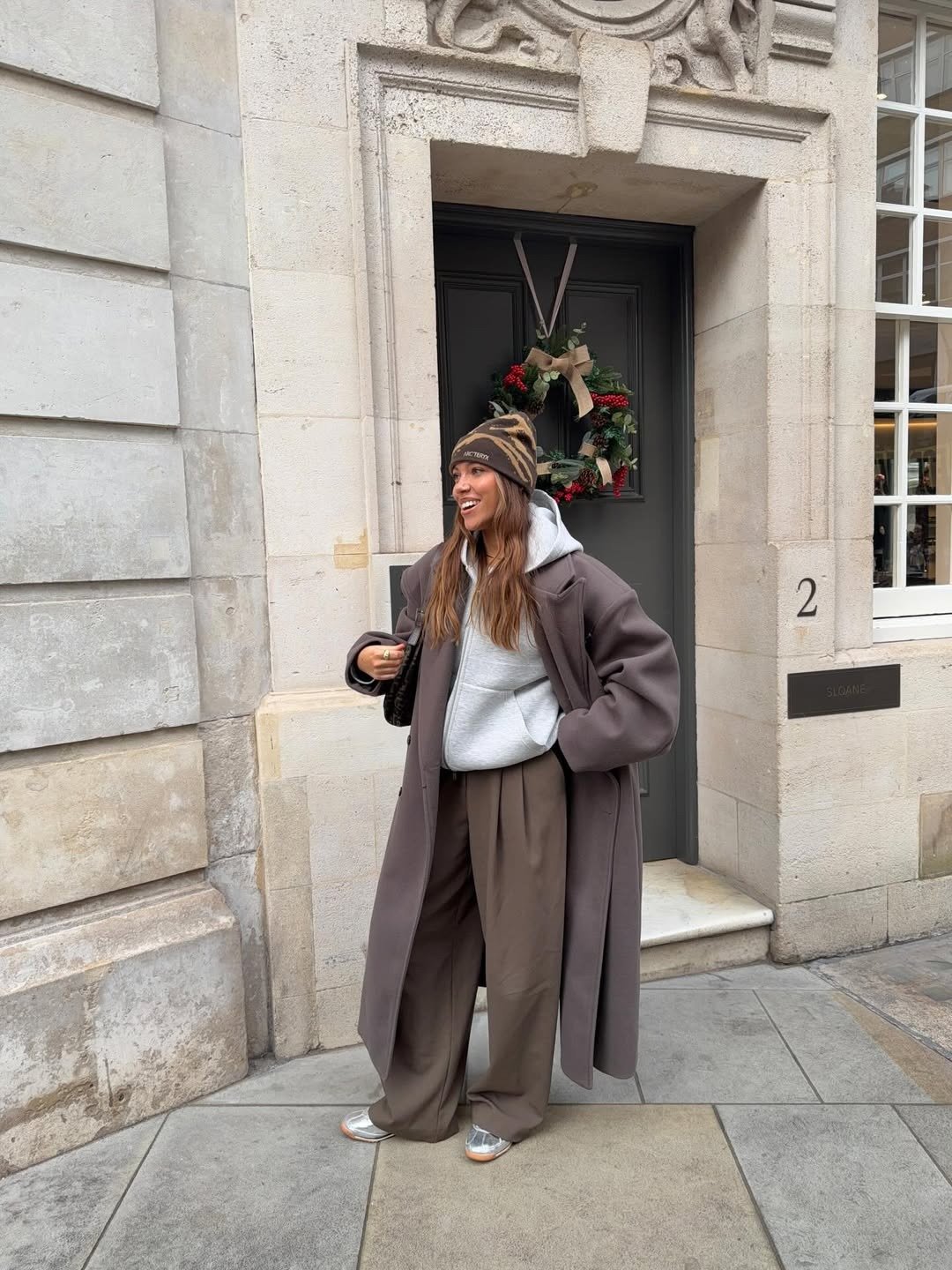 Modelos de calças de alfaiataria amplas em look marrom e cinza; modelo posa sorrindo diante de fachada elegante.