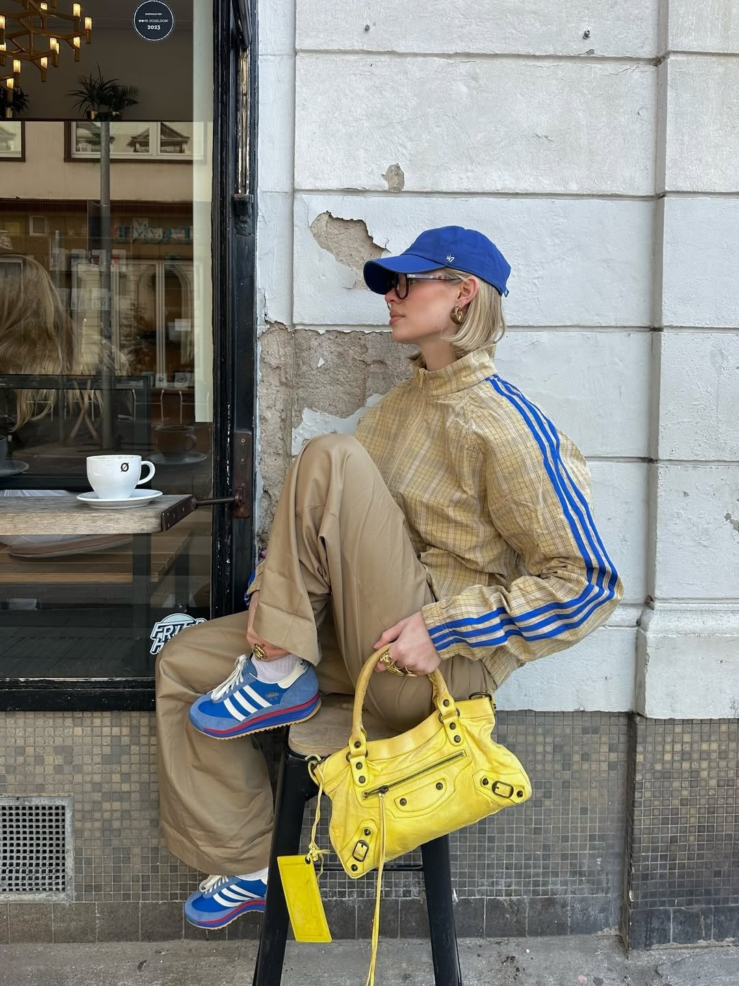 Looks estilosos para a variação de temperatura no outono com jaqueta bege, calça ampla, boné azul e bolsa amarela vibrante.