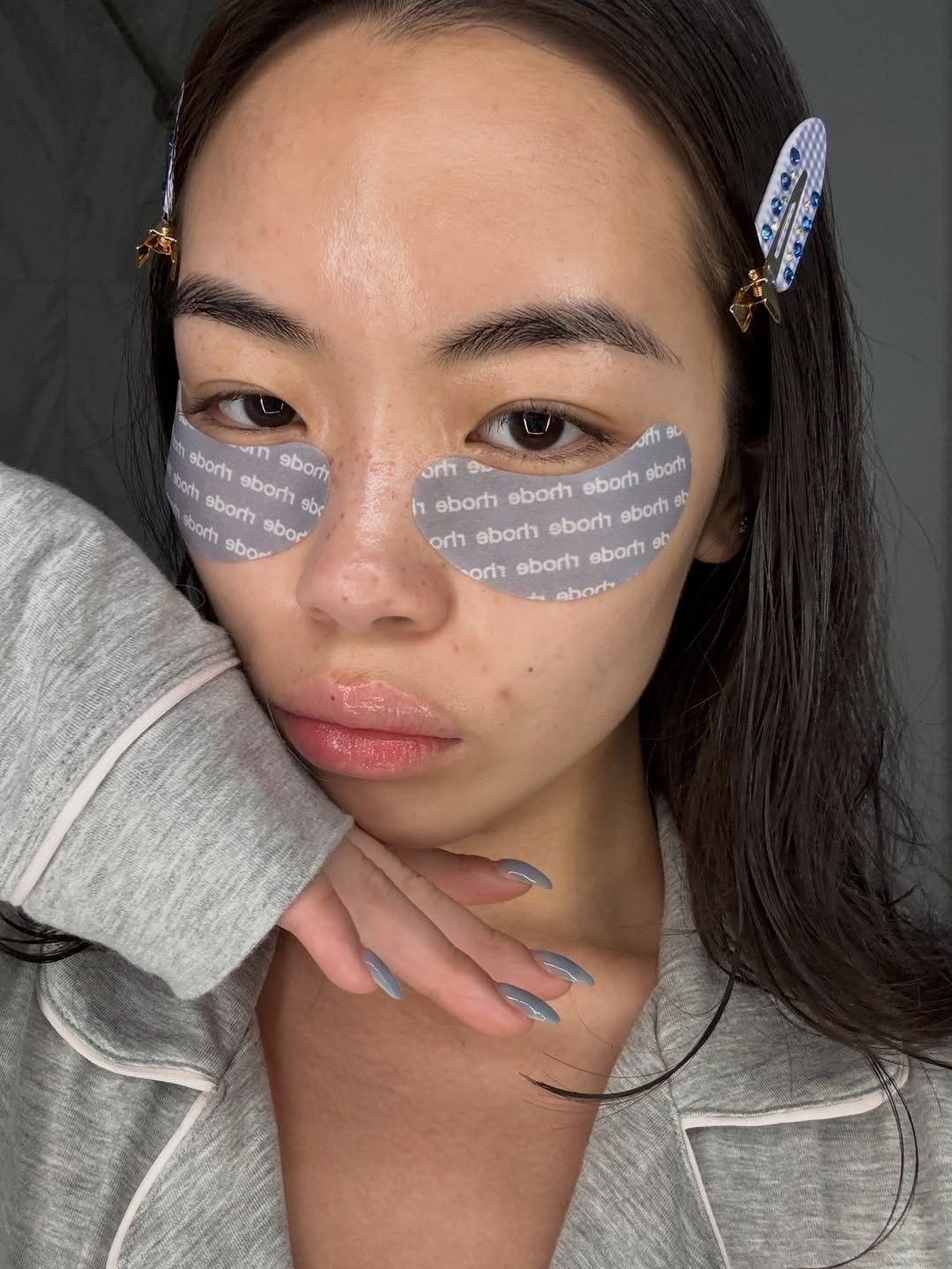 Benefícios da limpeza de pele em close sereno com pijama cinza, presilhas azuis e adesivos sob os olhos; Texto: rhode