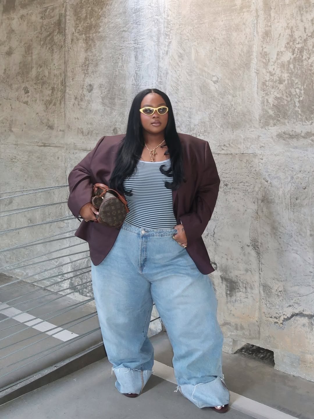 Looks para explorar a criatividade: modelo posa com blazer marrom, regata listrada e jeans amplo em clima urbano confiante.