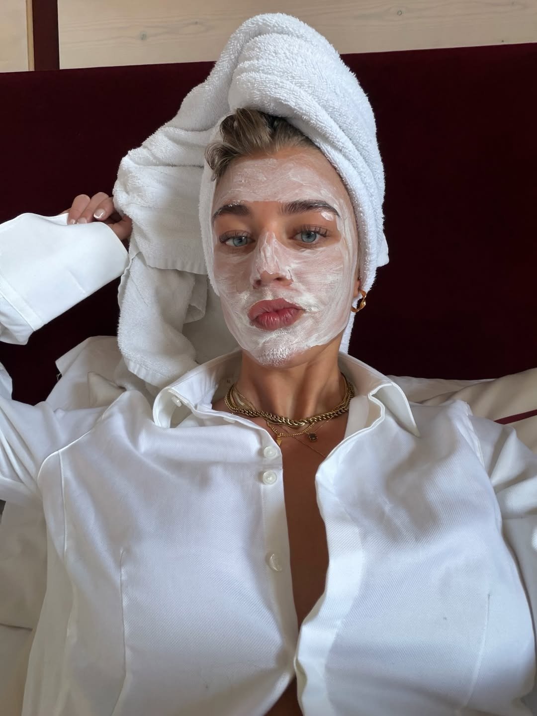 Ácido mandélico para que serve: modelo posa com toalha e máscara facial, camisa branca ampla e clima de autocuidado.