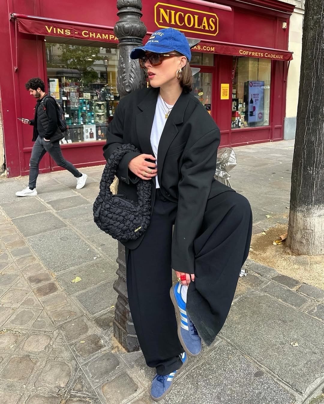 Modelos de calças de alfaiataria amplas em look preto; modelo posa com blazer oversized e boné azul.