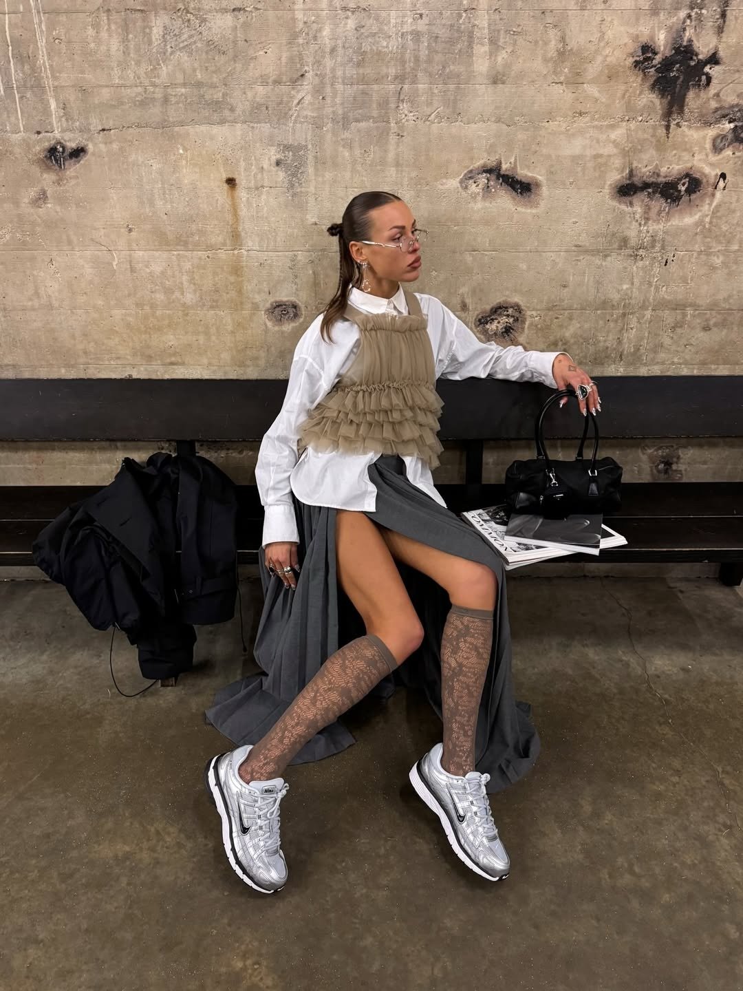 Looks estilosos para a variação de temperatura no outono com camisa branca, babados bege, saia cinza e tênis prata.