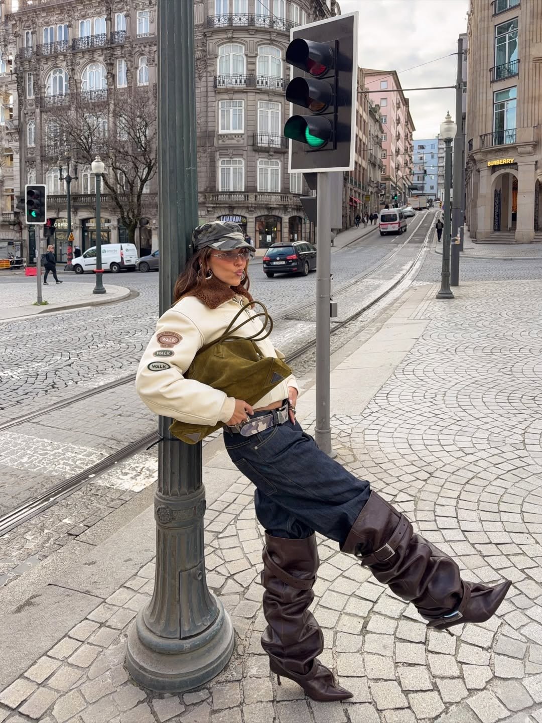 Looks para explorar a criatividade: modelo posa com jaqueta off-white, jeans amplo, botas drapeadas e bolsa verde na rua.