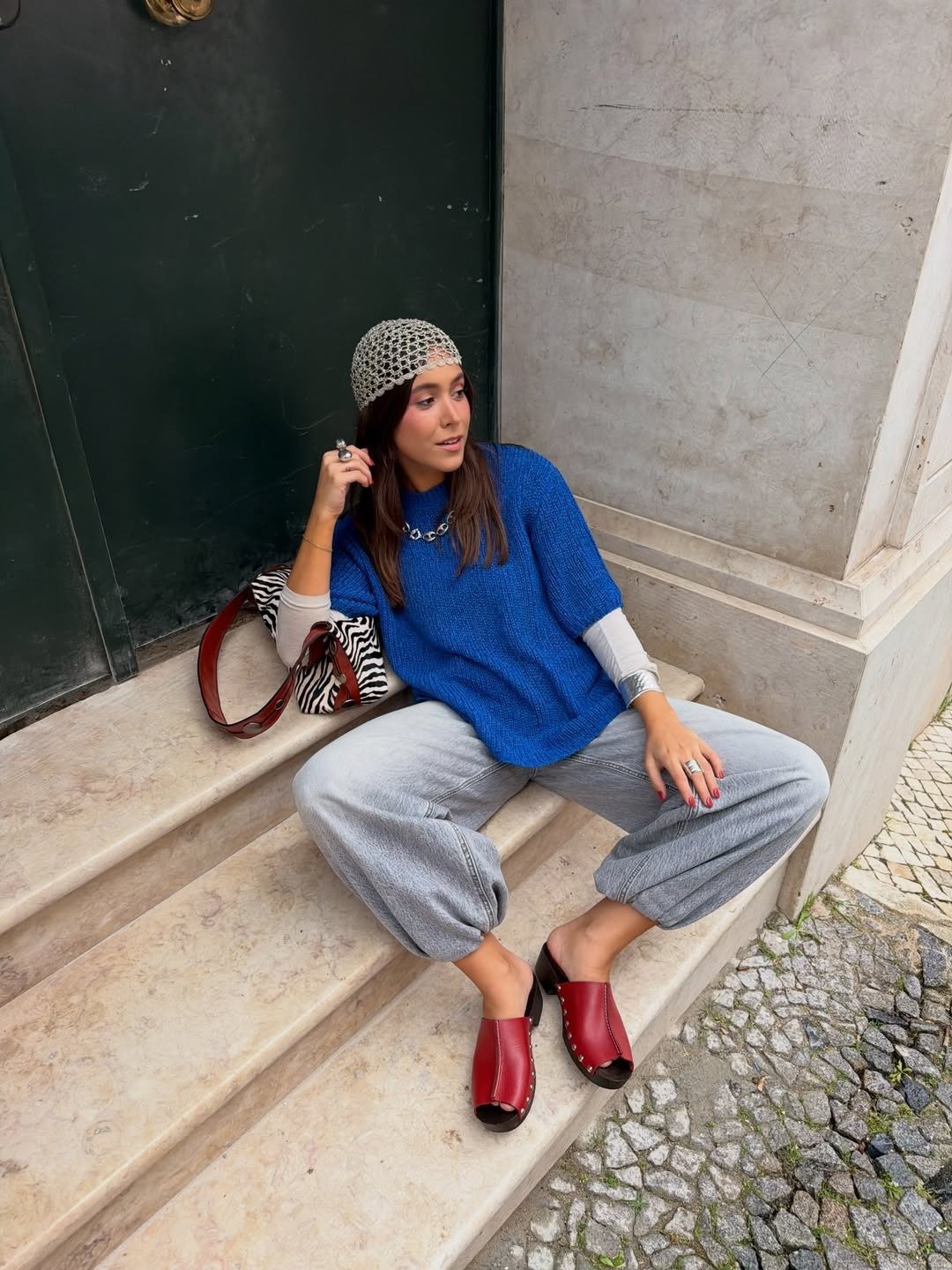 Looks estilosos para a variação de temperatura no outono: modelo posa com tricô azul, jeans amplo e clogs vinho.