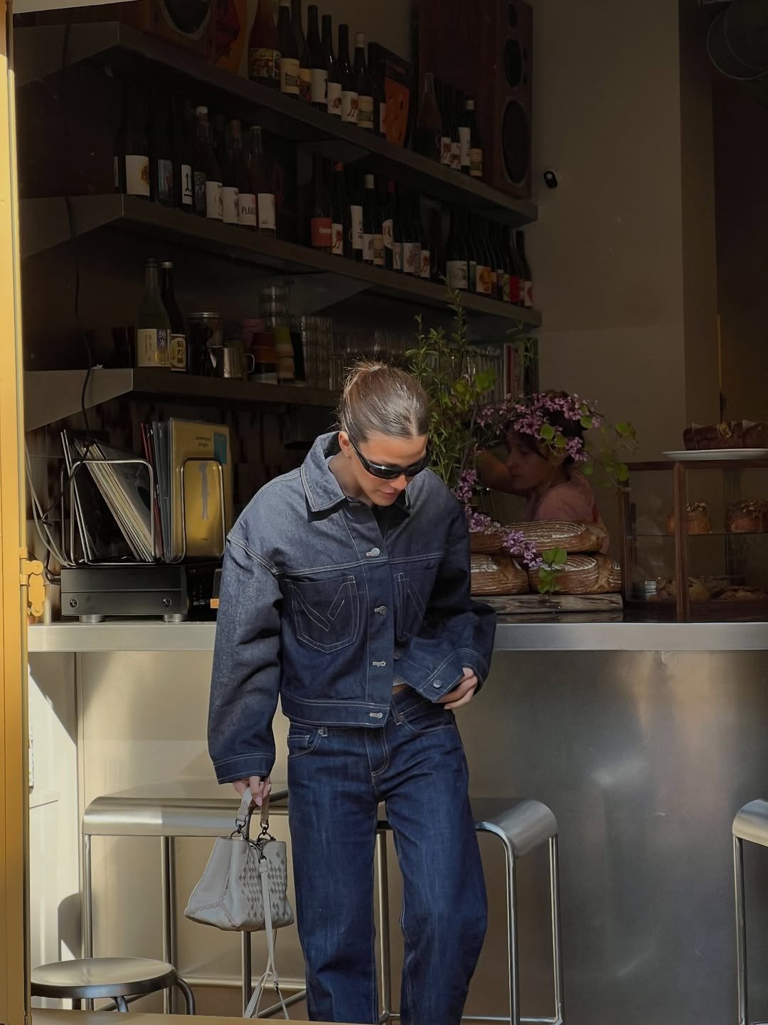 Looks estilosos para a variação de temperatura no outono com modelo posa em jeans escuro e óculos em café acolhedor
