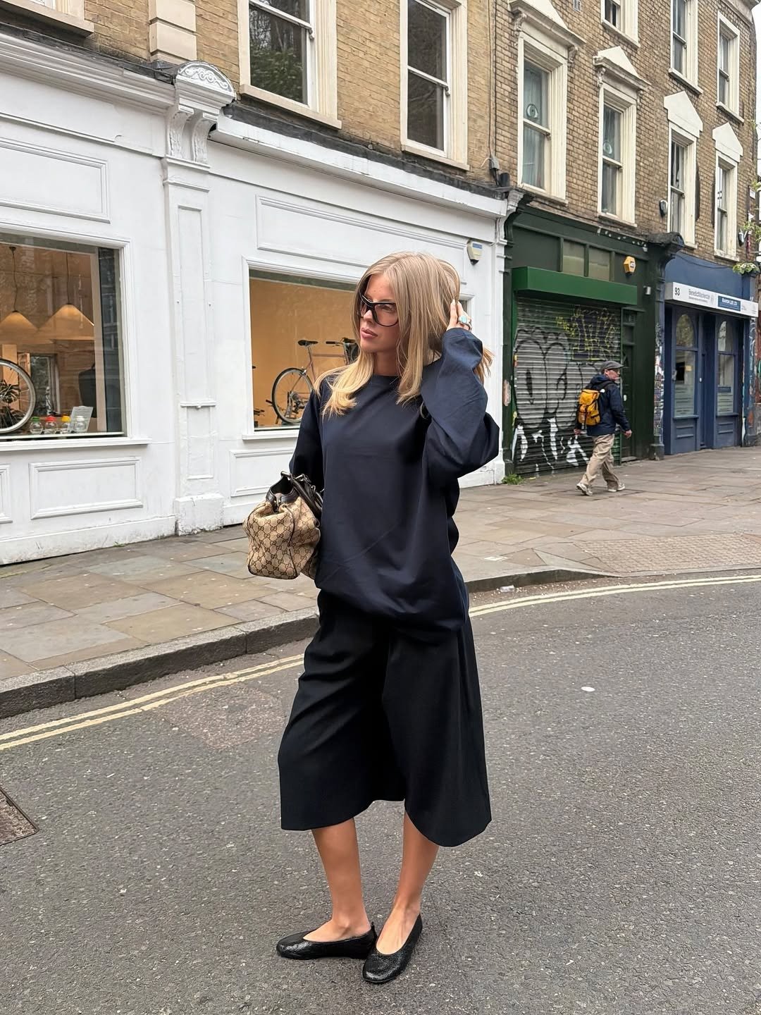 Looks estilosos para a variação de temperatura no outono: modelo posa com moletom amplo, pantacourt preta e sapatilha urbana.