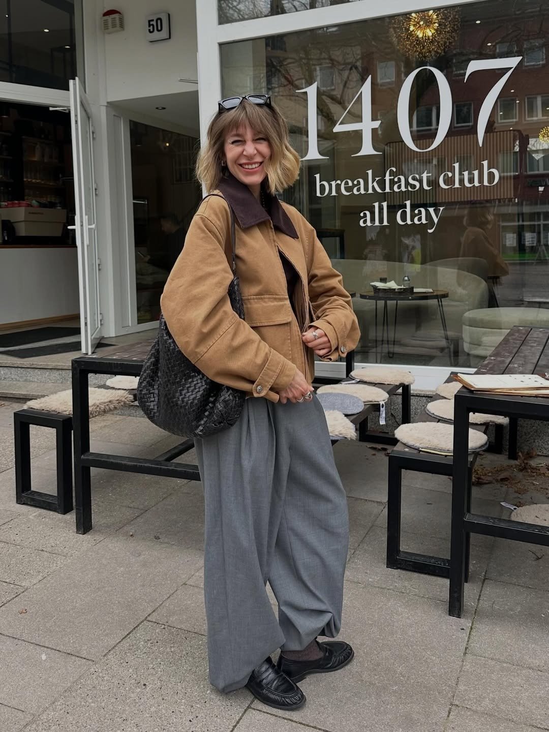 Modelos de calças de alfaiataria: modelo posa com calça cinza ampla, jaqueta caramelo e clima casual chic.