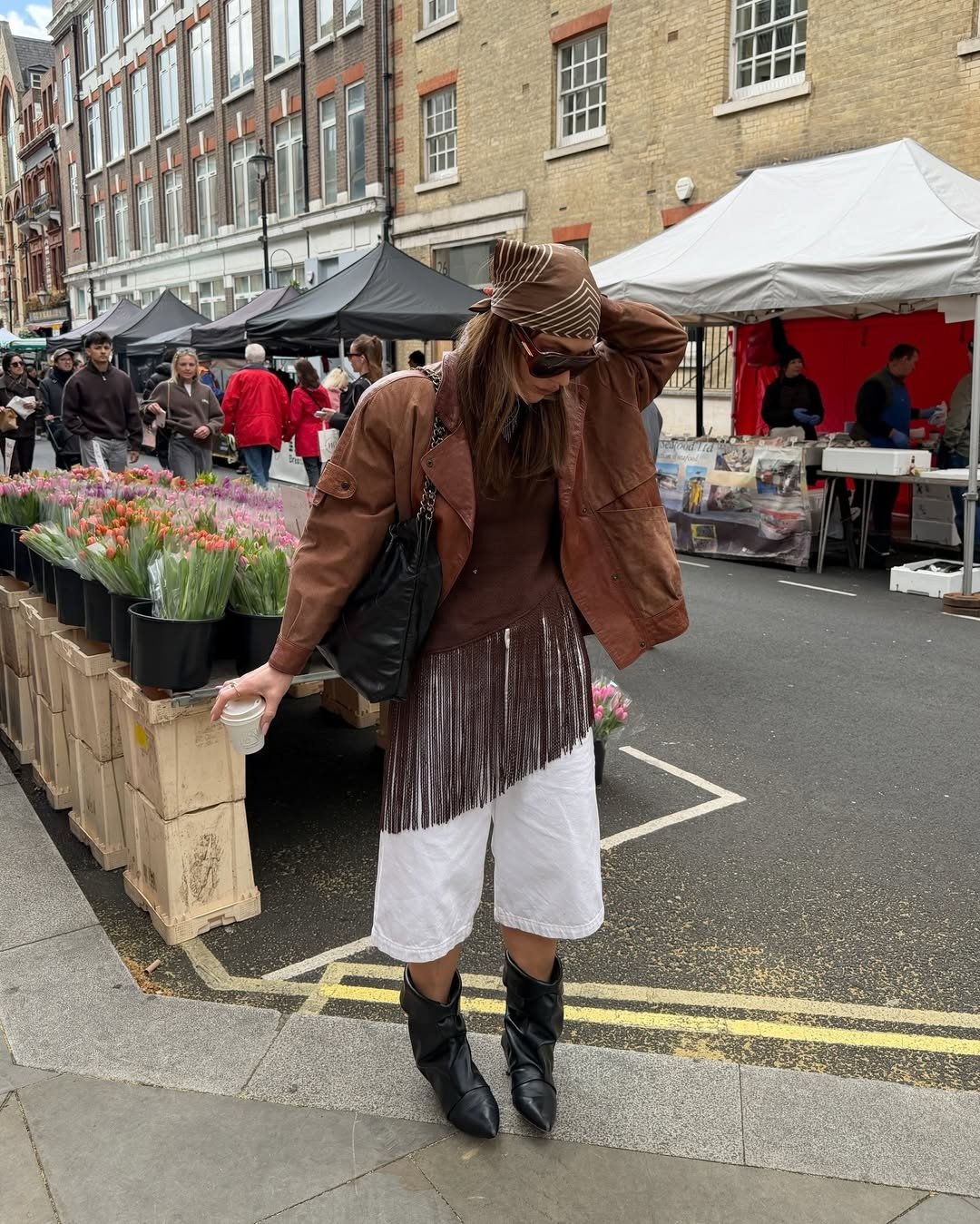 melhores sapatos para o outono: Modelo posa em feira urbana com jaqueta marrom, franjas e botas pretas de cano médio
