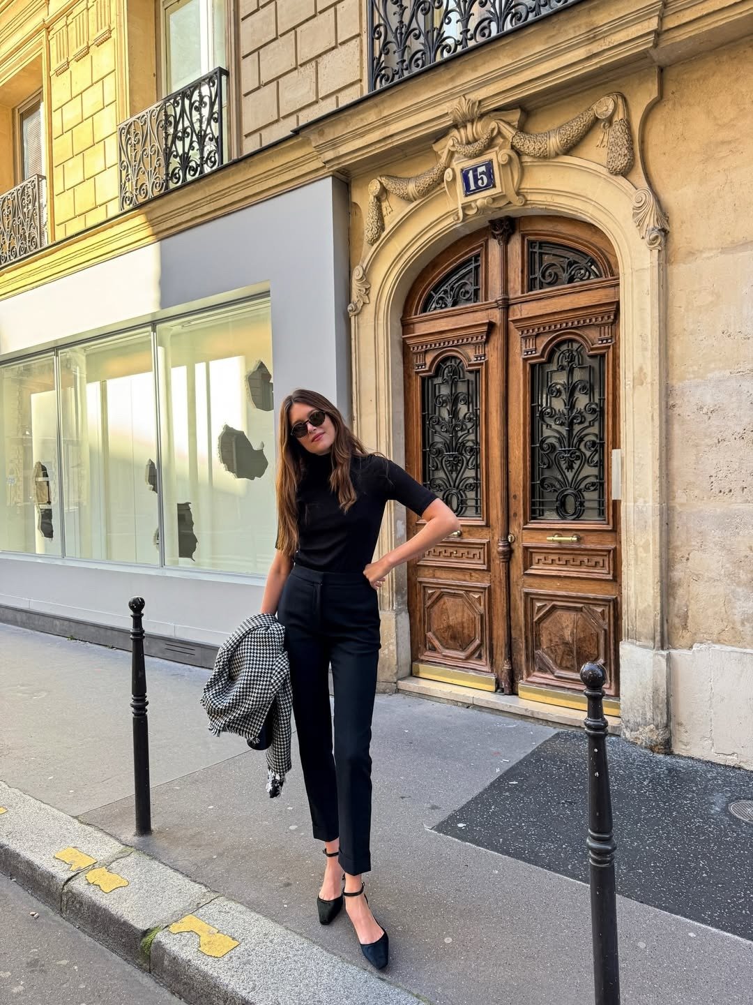 Modelos de calças de alfaiataria: modelo posa com corte reto preto, blusa ajustada e casaco pied-de-poule em rua elegante