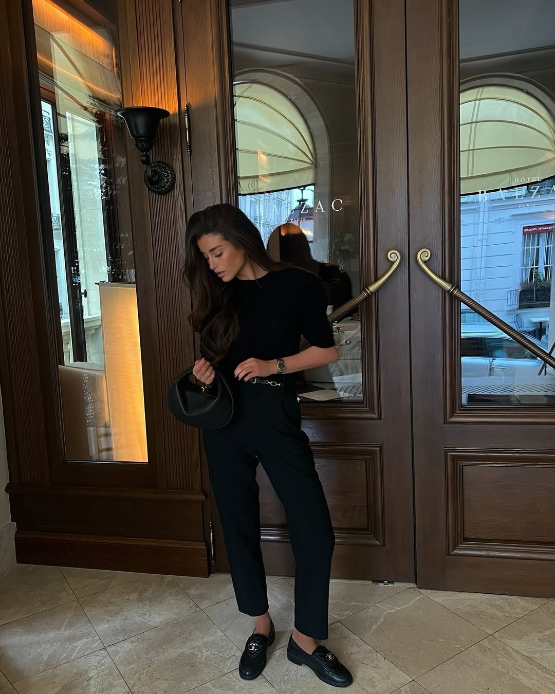 Modelos de calças de alfaiataria: modelo posa de preto com corte reto e clima sofisticado diante de portas de madeira.