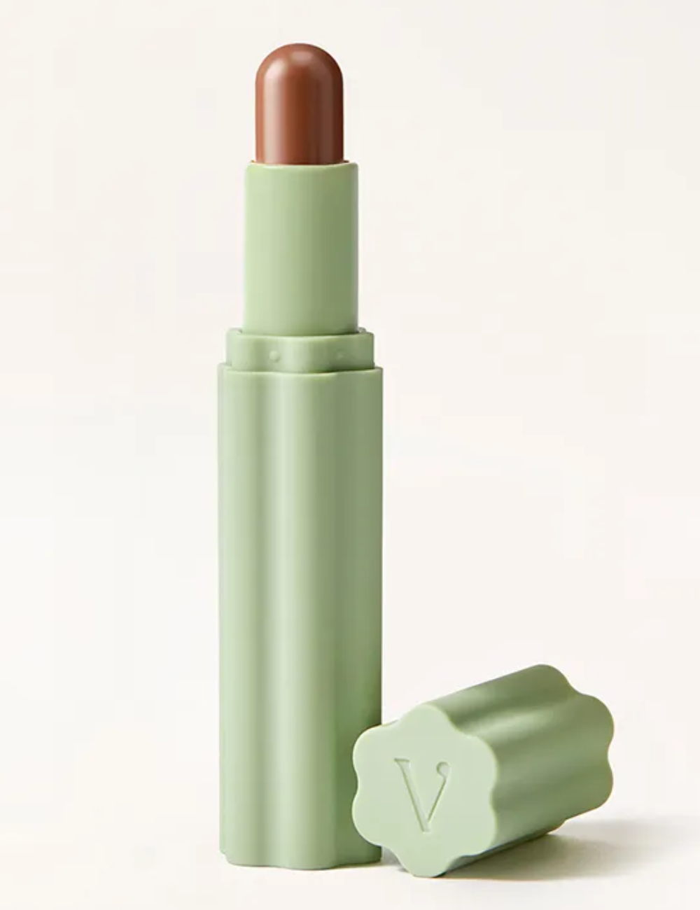 Sombras em stick marrom cintilante em embalagem verde-clara fosca com tampa floral, em fundo neutro elegante.