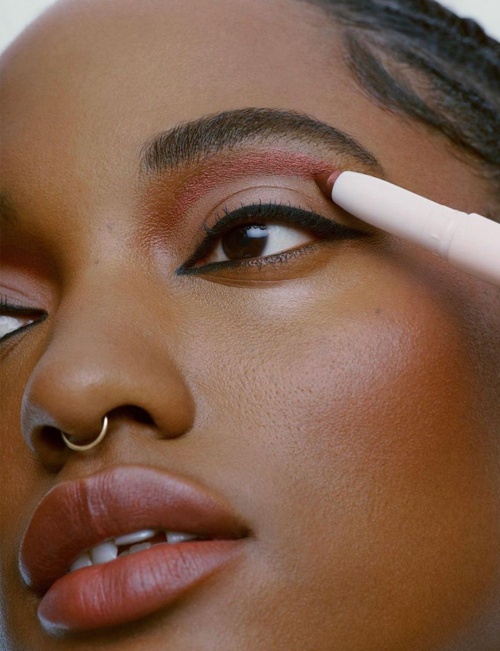 Sombras em stick rosé cintilante realçam o olhar da modelo em close com delineado preto, pele luminosa e clima sofisticado